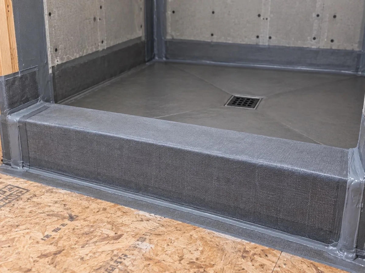 A shower curb wrapped in waterproofing membrane on three sides, the framing step that separates a straightforward curbless conversion from a major rebuild