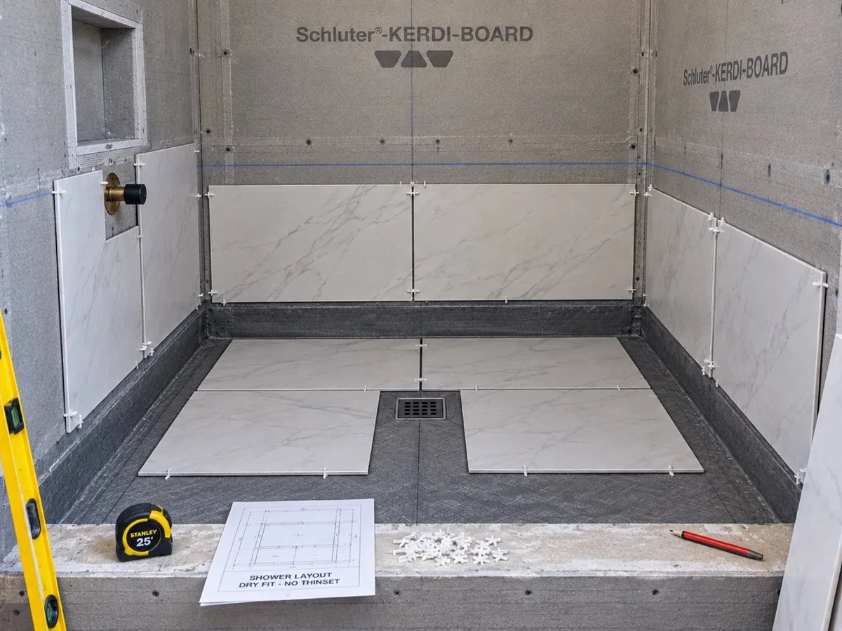 Mid-build: large format tile dry-fitted on the shower floor and walls with spacers and chalk lines, before any thinset goes down