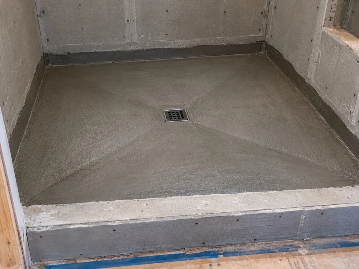 Mid-build: a poured cement shower base, shaped by hand to fall to the drain, with cement backer board walls and a wrapped curb