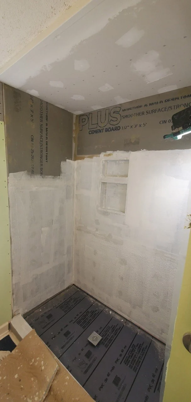 Cement backer board screwed to shower studs on the left next to ordinary drywall on the right, marked as the wrong substrate for tile