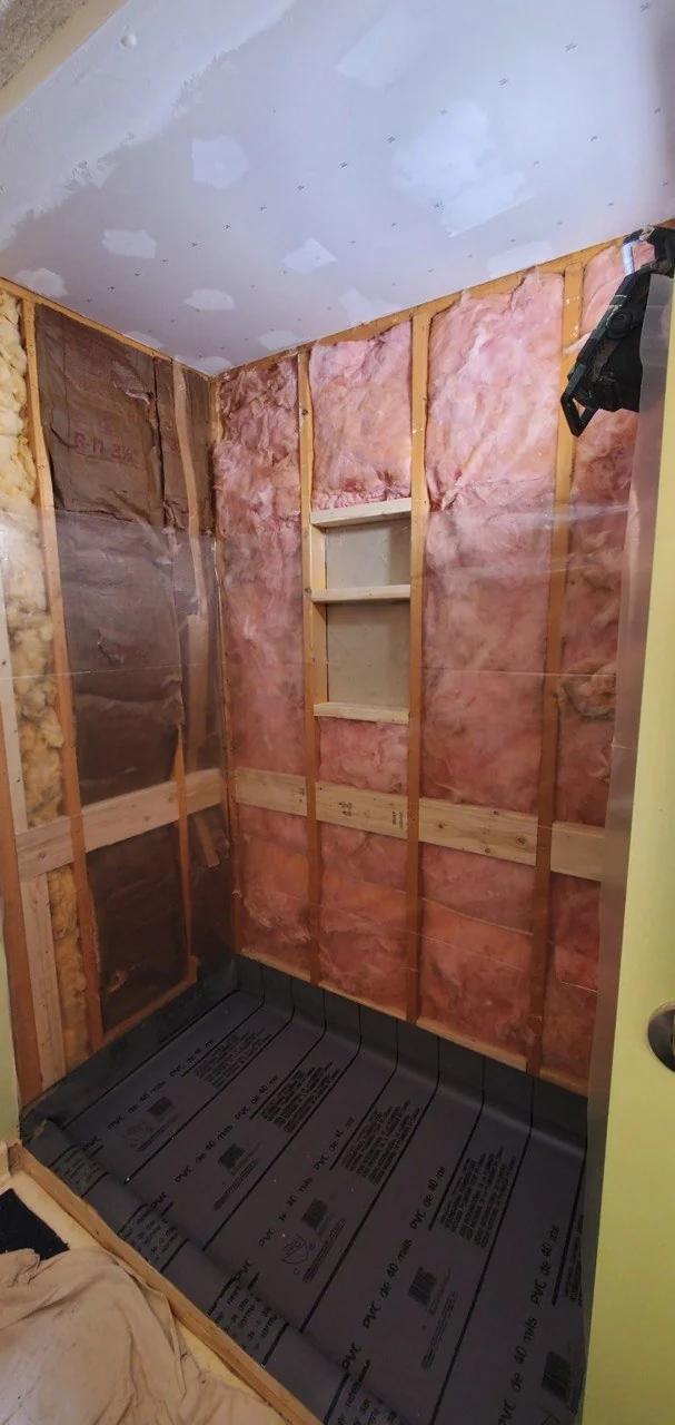 One of our showers opened to the studs: the niche framed and blocked between two studs, insulation in the walls, plastic over the raw framing and the pan liner already down on the floor