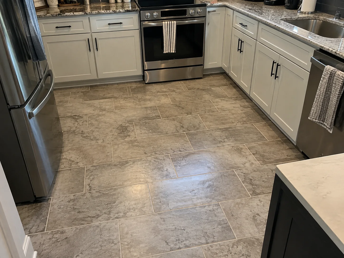 A tiled kitchen floor in large-format stone-look porcelain laid in an offset pattern, with the cabinets, range, dishwasher and refrigerator back in place