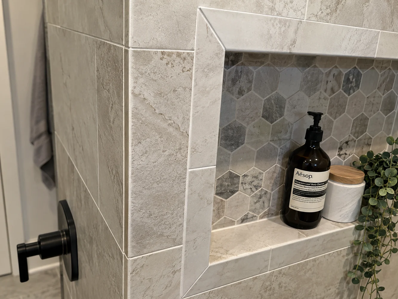 A tiled shower niche framed with mitered tile on all four sides, backed with hex mosaic and finished with a sloped sill